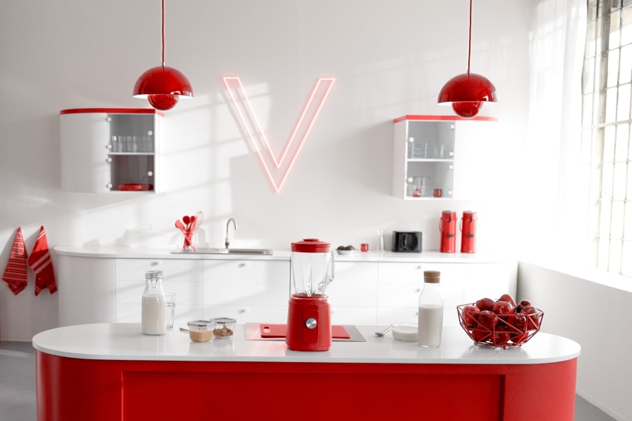 Roter Mixer mit Milch und frischen Beeren auf einer modernen weiß-roten Küchenarbeitsplatte