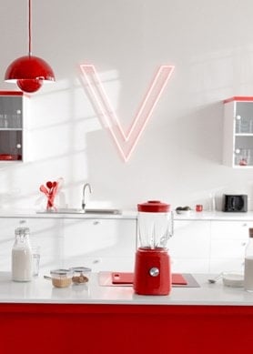 Roter Mixer mit Milch und frischen Beeren auf einer modernen weiß-roten Küchenarbeitsplatte