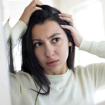 Junge Frau prüft im Spiegel ihre Kopfhaut und wirkt besorgt über Haarausfall