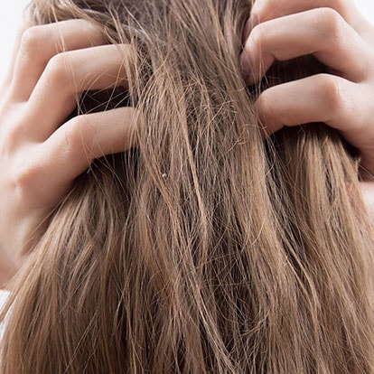 Frau mit langen, dunkelblonden Haaren von hinten kratzt sich an der Kopfhaut