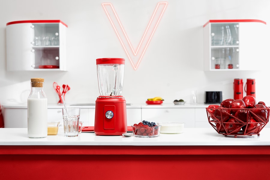 Eine rote Küche mit rotem Hochleistungsmixer, Obst und einem leuchtenden V an der Wand.