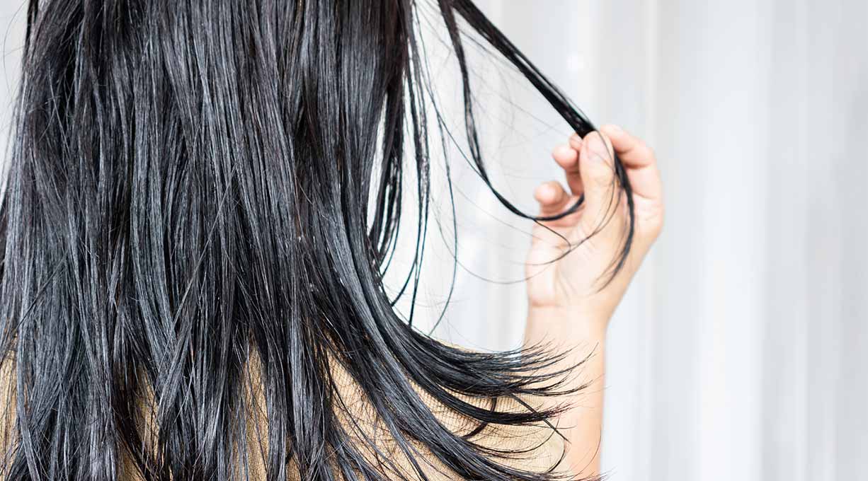Frau mit dunklen langen Haaren hält eine Strähne in der Hand