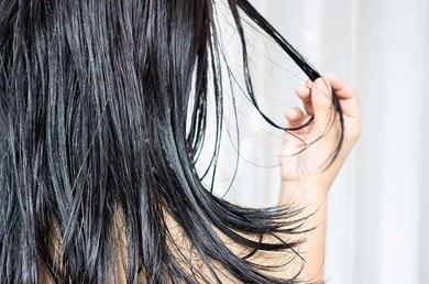 Frau mit dunklen langen Haaren hält eine Strähne in der Hand