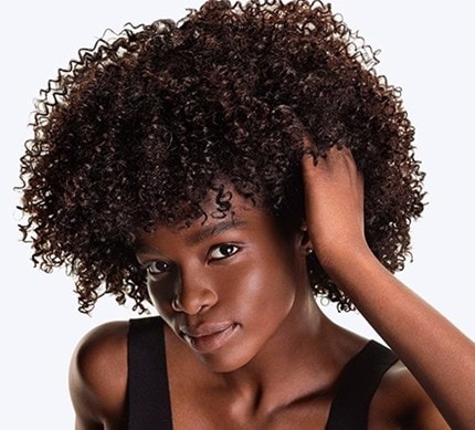 Nahaufnahme eines dunkelhaarigen, weiblichen Models mit Locken, das sich in die Haare greift