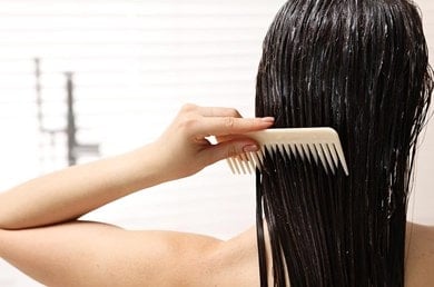 Frau mit dunklen Haaren von hinten, die sich die Haare mit einem Kamm kämmt