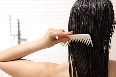Frau mit dunklen Haaren von hinten, die sich die Haare mit einem Kamm kämmt