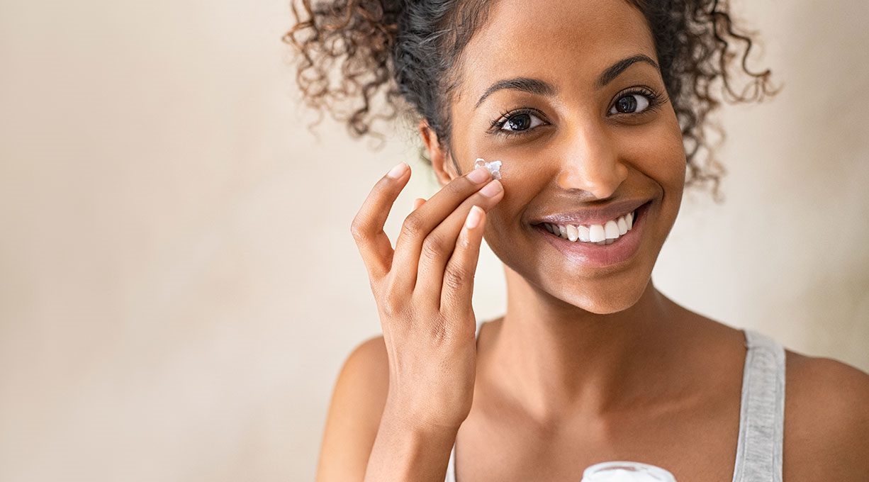 Eine junge Schwarze Frau, die sich Creme auf die Wange aufträgt