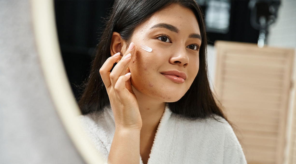 Eine Frau schaut zur Seite und tupft sich Creme auf ihr Gesicht.