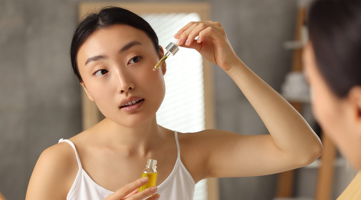 Eine Frau schaut in den Spiegel und träufelt Serum auf ihr Gesicht.