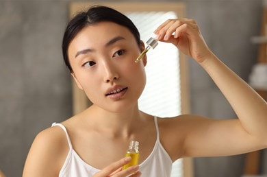 Eine Frau steht vor dem Spiegel und trägt Retinol-Serum mit einer Pipette auf dem Gesicht auf