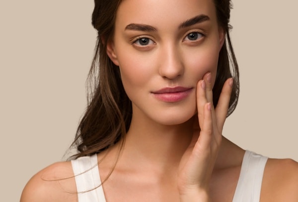 Junge Frau mit dunklen Haaren berührt ihre Wange mit zwei Fingern