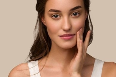 Junge Frau mit dunklen Haaren berührt ihre Wange mit zwei Fingern