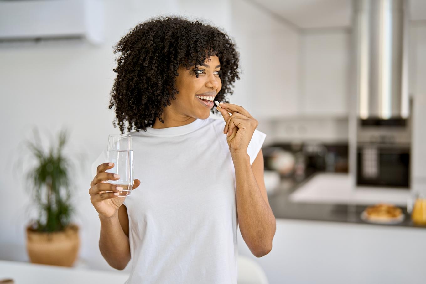 Frau nimmt in der Küche eine Kollagen-Kapsel mit einem Glas Wasser ein