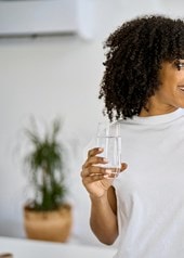 Frau nimmt in der Küche eine Kollagen-Kapsel mit einem Glas Wasser ein