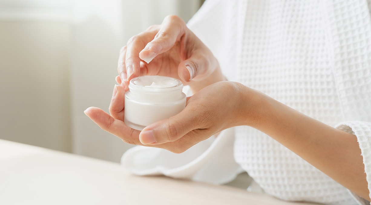 Eine Frau hält einen Tiegel Creme in der Hand und entnimmt ein wenig Creme mit dem Finger