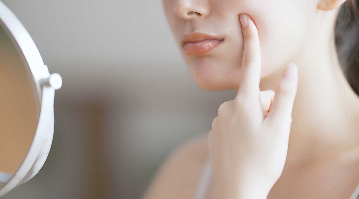 Mundpartie einer Frau, die ihren Finger auf die Wange hält