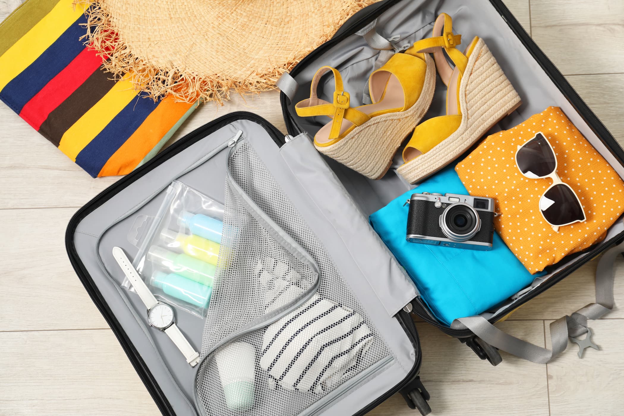 Geöffneter Koffer mit Sommerkleidung, Sandalen, Sonnenbrille und Reiseaccessoires für den Urlaub