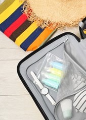 Geöffneter Koffer mit Sommerkleidung, Sandalen, Sonnenbrille und Reiseaccessoires für den Urlaub