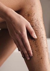 Ausschnitt von Beinen einer Frau die sich die Wade mit einem dunklen Peeling einreibt