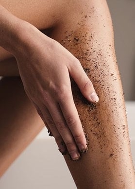 Ausschnitt von Beinen einer Frau die sich die Wade mit einem dunklen Peeling einreibt