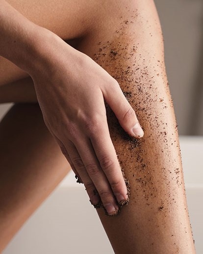 Ausschnitt von Beinen einer Frau die sich die Wade mit einem dunklen Peeling einreibt
