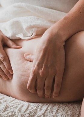 Frau im Sitzen drückt ihre Haut am Oberschenkel so zusammen, dass Cellulite entsteht