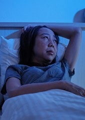 Frau liegt nachts wach im Bett wegen Nachtschweiß neben einem schlafenden Kind