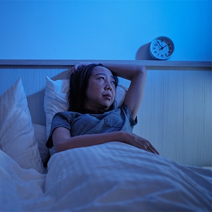 Frau liegt nachts wach im Bett wegen Nachtschweiß neben einem schlafenden Kind