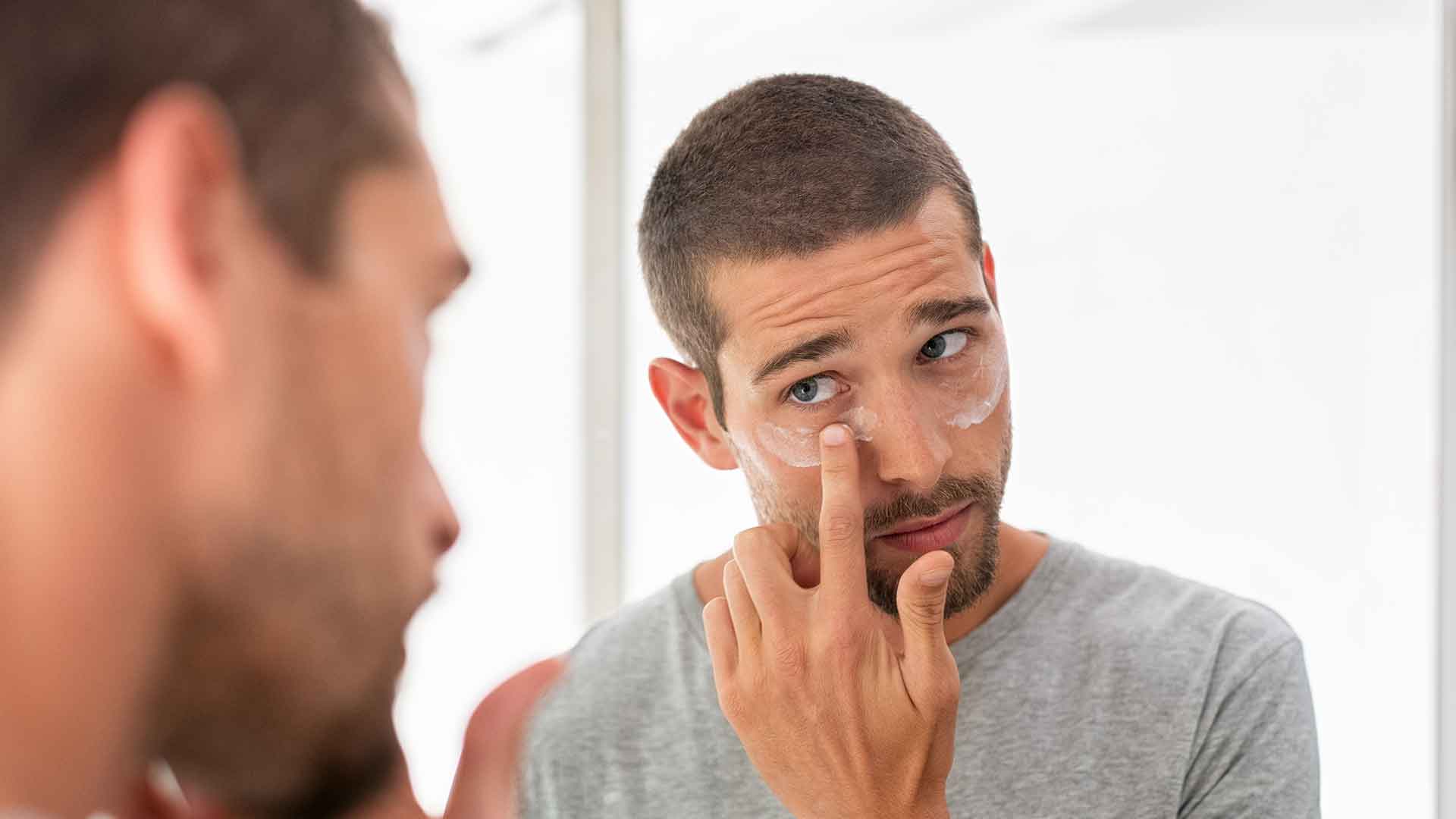 Mann mit Bart und kurzen Haaren trägt Feuchtigkeitspflege unter den Augen auf
