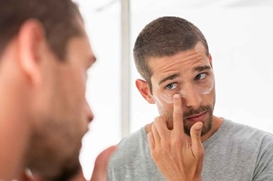 Mann mit Bart und kurzen Haaren trägt Feuchtigkeitspflege unter den Augen auf