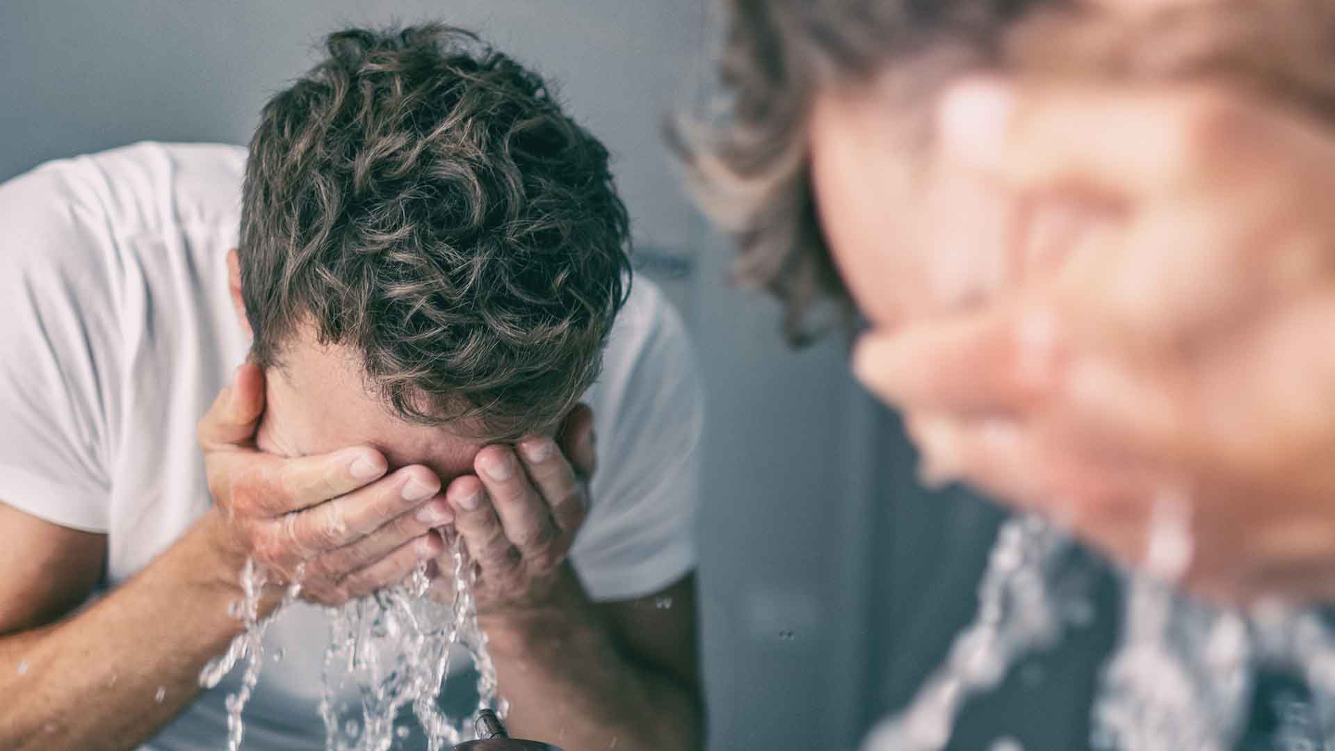 Ein Mann steht vor dem Spiegel und gibt sich Wasser ins Gesicht
