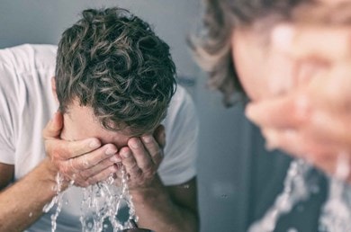 Ein Mann steht vor dem Spiegel und gibt sich Wasser ins Gesicht