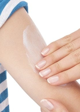 Eine Hand trägt weiße Creme auf den Arm einer Person mit blau-weiß gestreiftem Shirt auf, um die Haut zu pflegen und Feuchtigkeit zu spenden.
