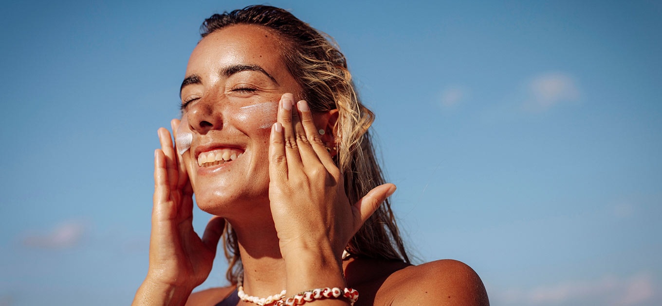 Frau cremt ihr Gesicht in der Sonne ein, blauer Himmel im Hintergrund