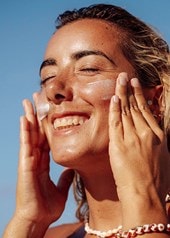 Frau cremt ihr Gesicht in der Sonne ein, blauer Himmel im Hintergrund