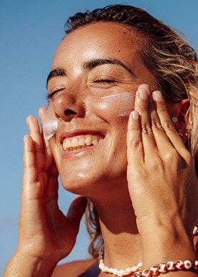 Frau cremt ihr Gesicht in der Sonne ein, blauer Himmel im Hintergrund