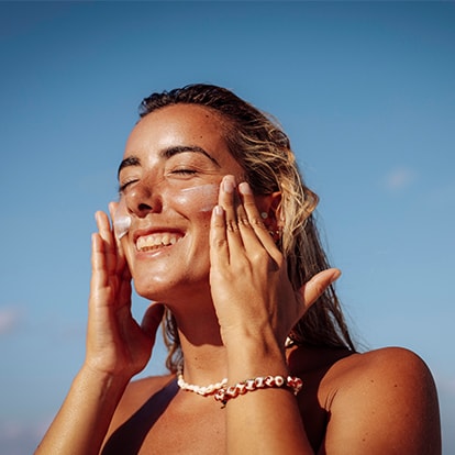 Frau cremt ihr Gesicht in der Sonne ein, blauer Himmel im Hintergrund