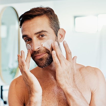Mann trägt Sonnencreme im Badezimmer im Gesicht auf
