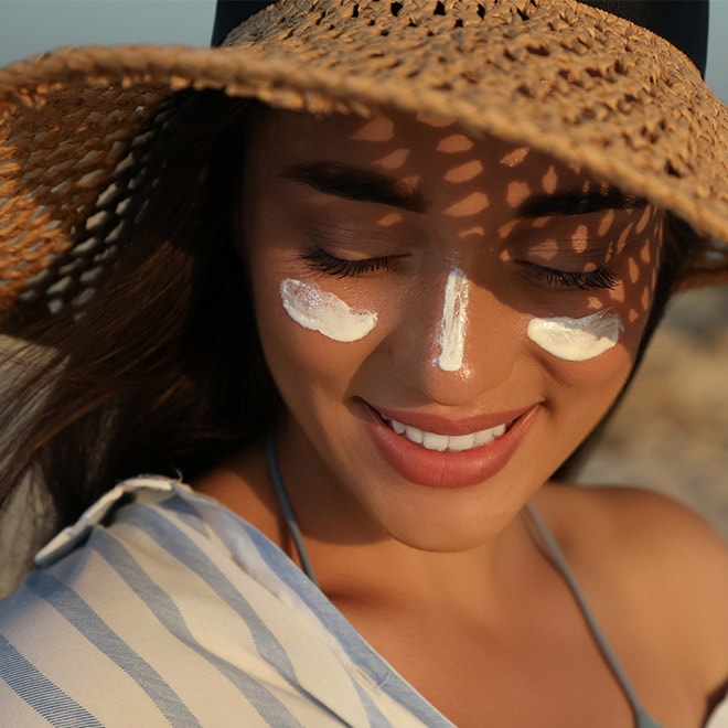Junge Frau mit Streifen aus Sonnencreme auf Wange und Nase und einem Strohhut