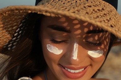 Junge Frau mit Streifen aus Sonnencreme auf Wange und Nase und einem Strohhut