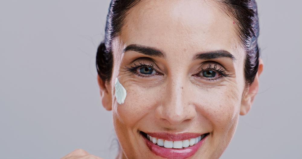 Lächelnde Frau mit aufgetragener Sonnencreme auf der Wange