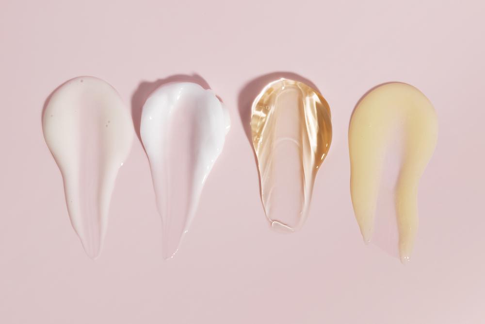 Verschiedene Hautpflegeprodukte wie Creme, Gel und Serum auf rosa Hintergrund