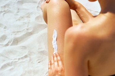 Rückenansicht einer Person, die ihr linkes Bein mit Sonnencreme eincremt, um sich vor UVA-Strahlen zu schützen