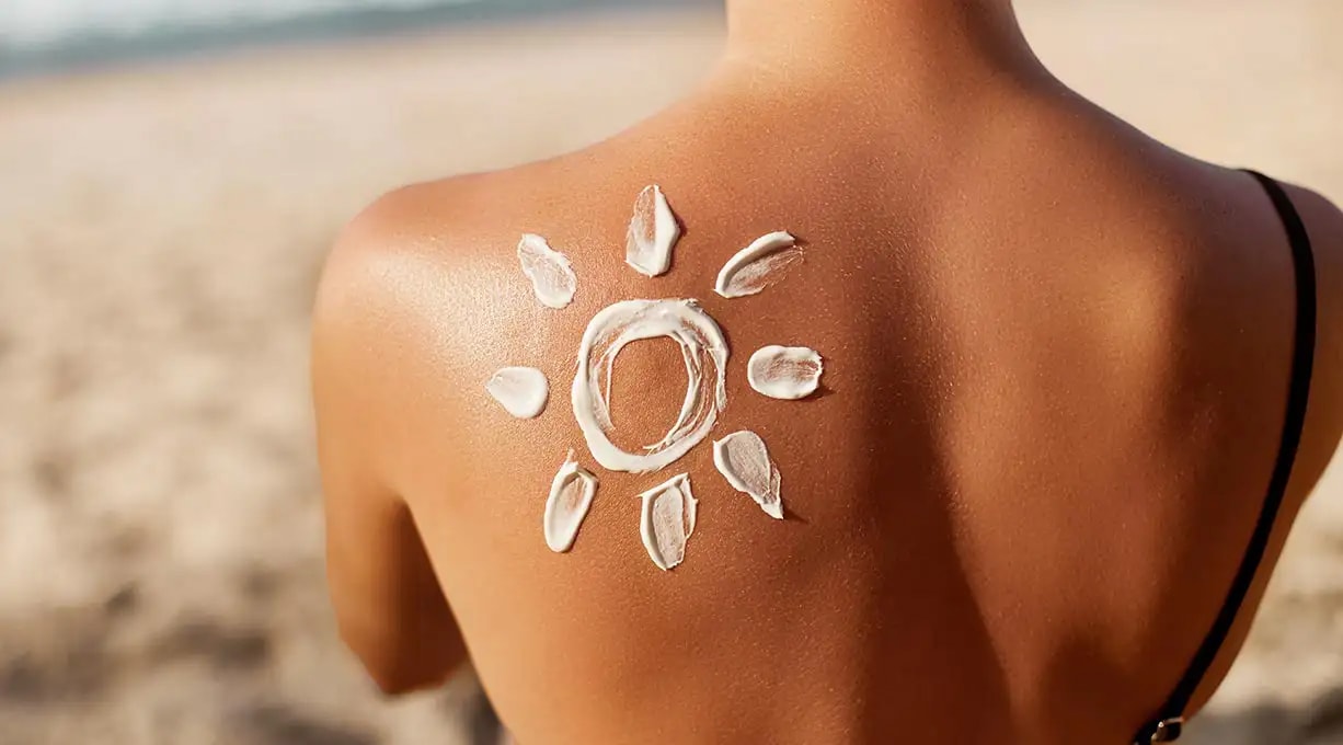 Aufnahme des oberen Rücken einer Frau, auf dessen linken schulter eine Sonne mit Sonnencreme gemalt 