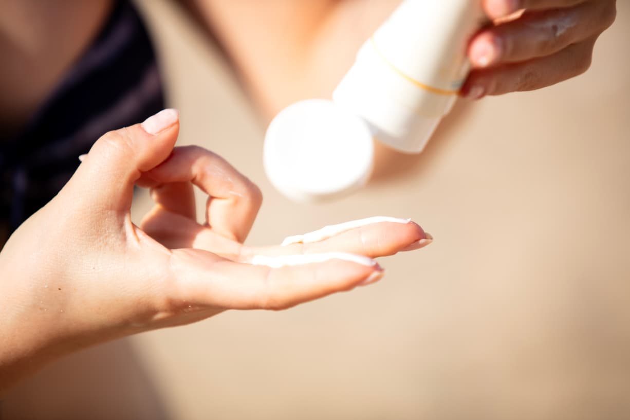 Hand, auf die Sonnencreme aus einer Tube dosiert wird