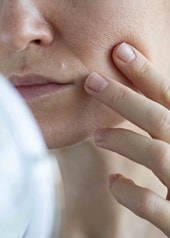 Frau berührt die Wange und prüft ihre großporige Haut im Spiegel