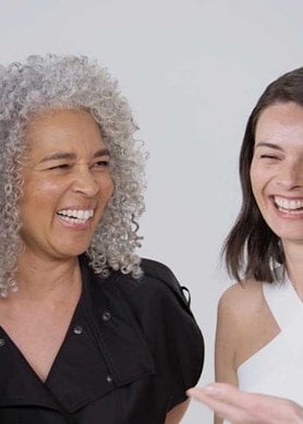 Vier Personen stehen in einer Gruppe, tragen stylische Kleidung und lachen zusammen.