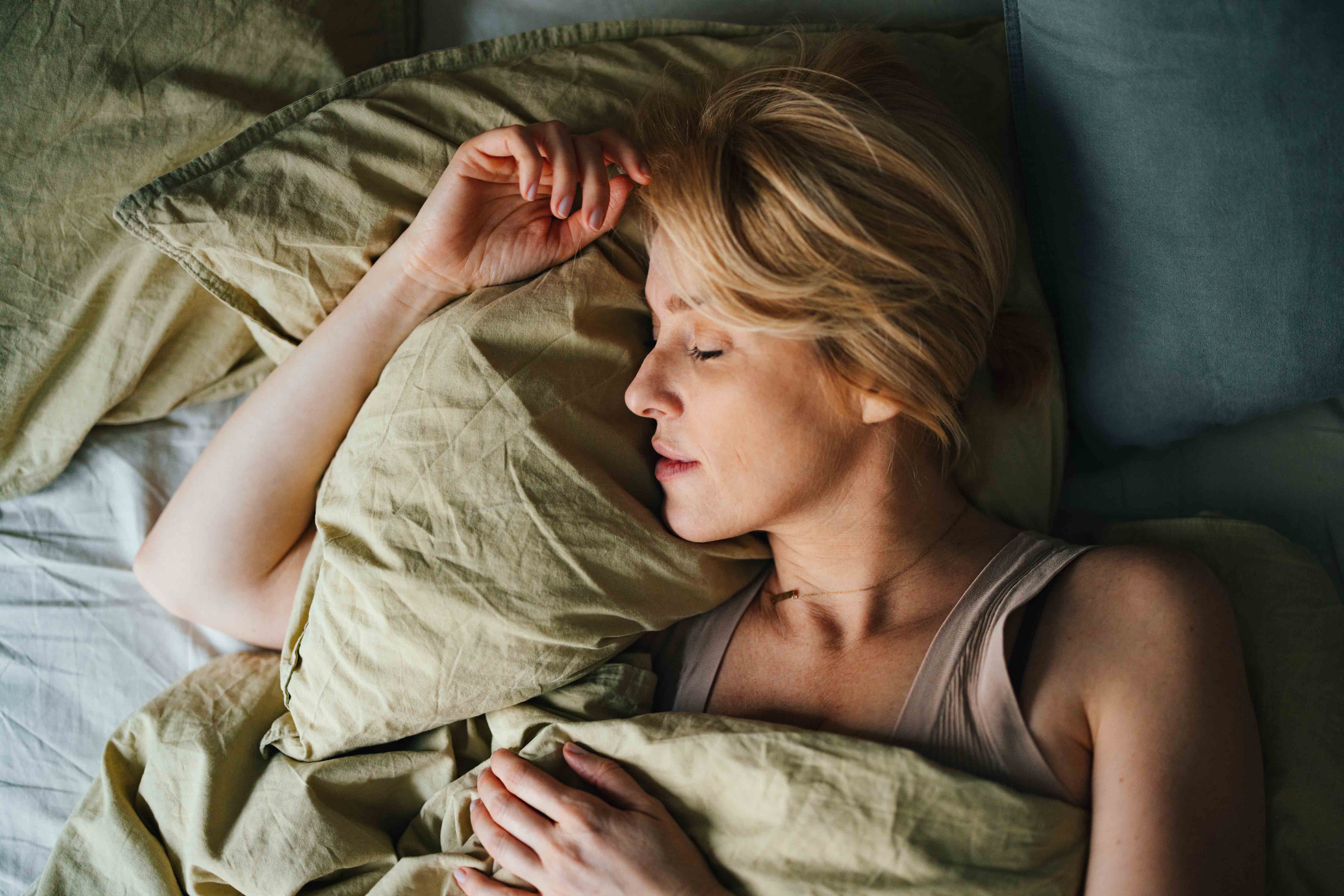 Frau mittleren Alters schläft im Bett unter einer grünen Bettdecke
