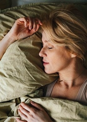 Frau mittleren Alters schläft im Bett unter einer grünen Bettdecke