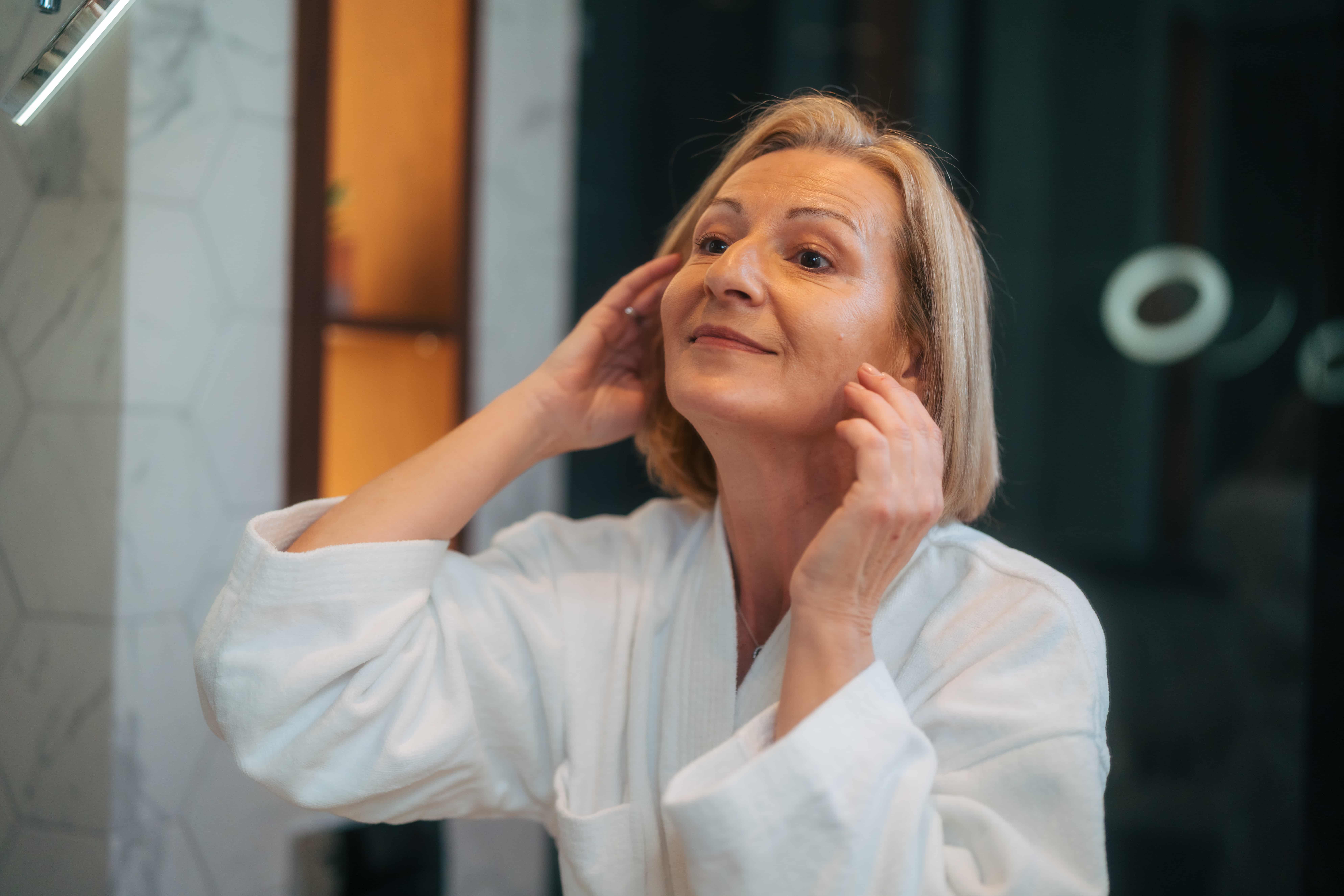 Frau in den Wechseljahren berührt ihr Gesicht im Badezimmer